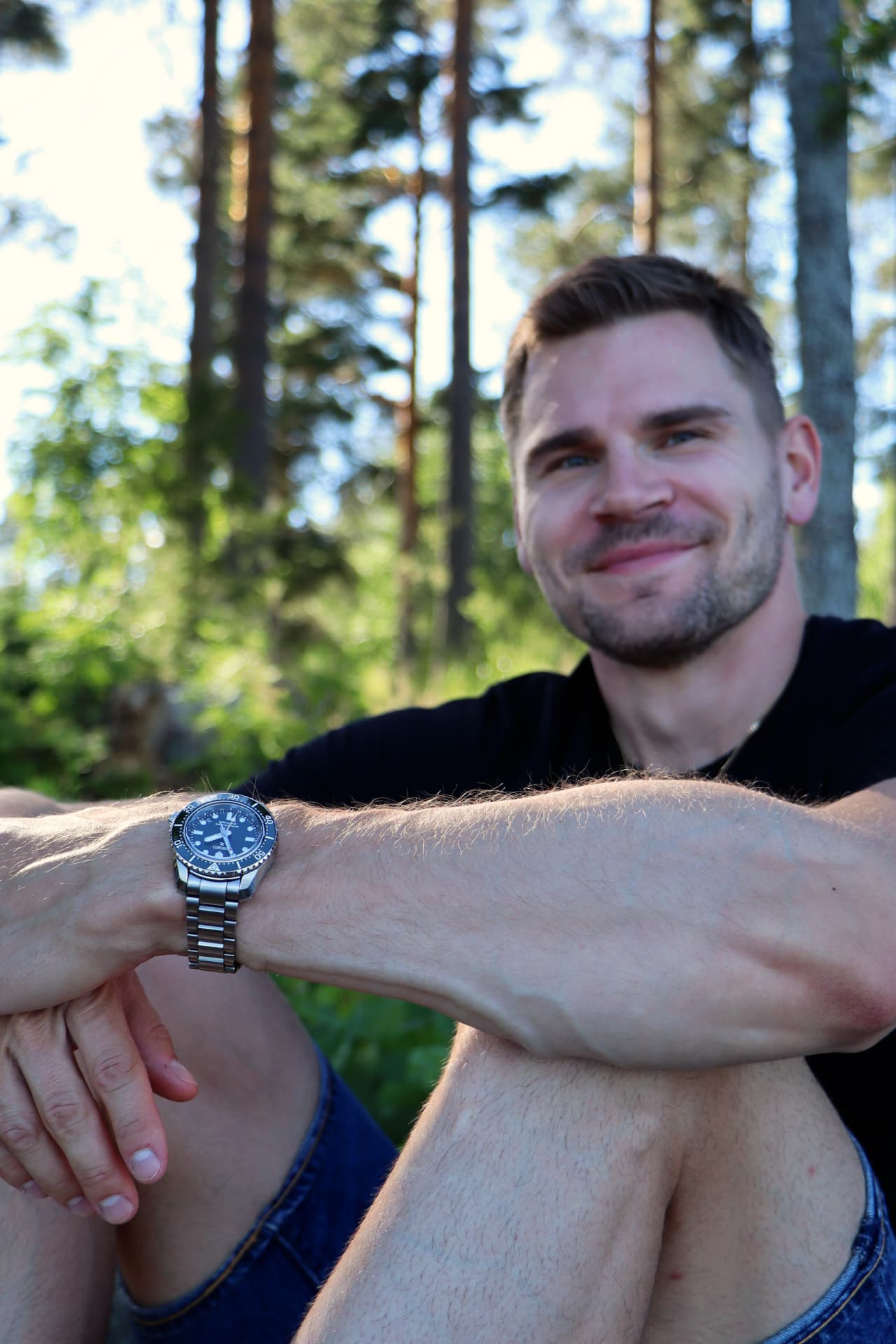 Elmo Lakka sitting in a forest showing the watch on his wrist.